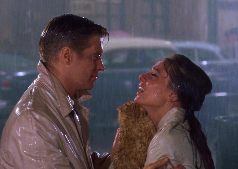 A man and a woman looking at each other in the rain while the woman cries and holds a cat.