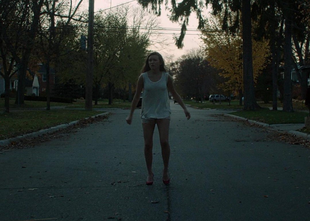A troubled looking girl with shorts, a tank top and high heels on in the middle of the street.