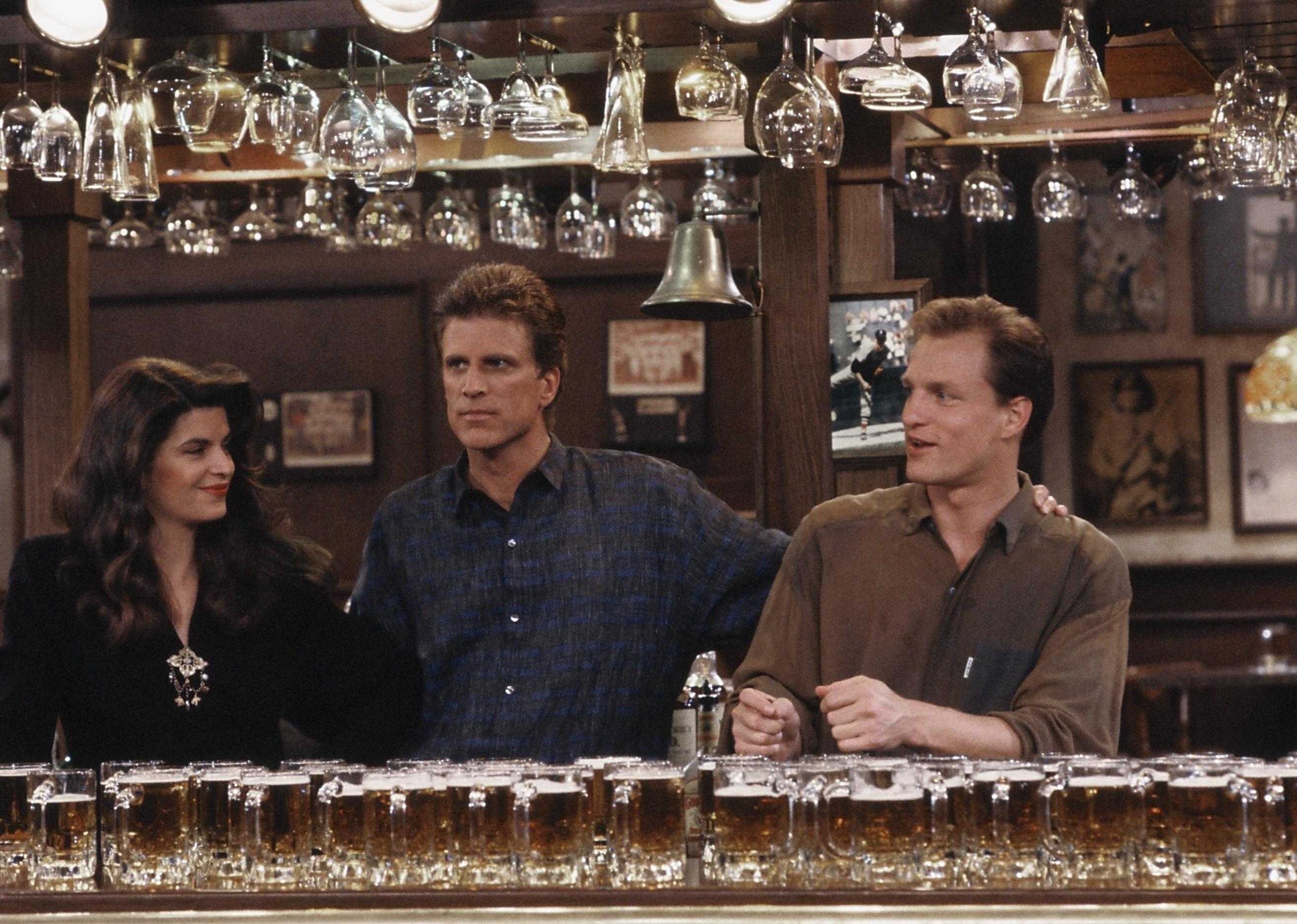 Kirstie Alley, Woody Harrelson, and Ted Danson smiling behind a bar.