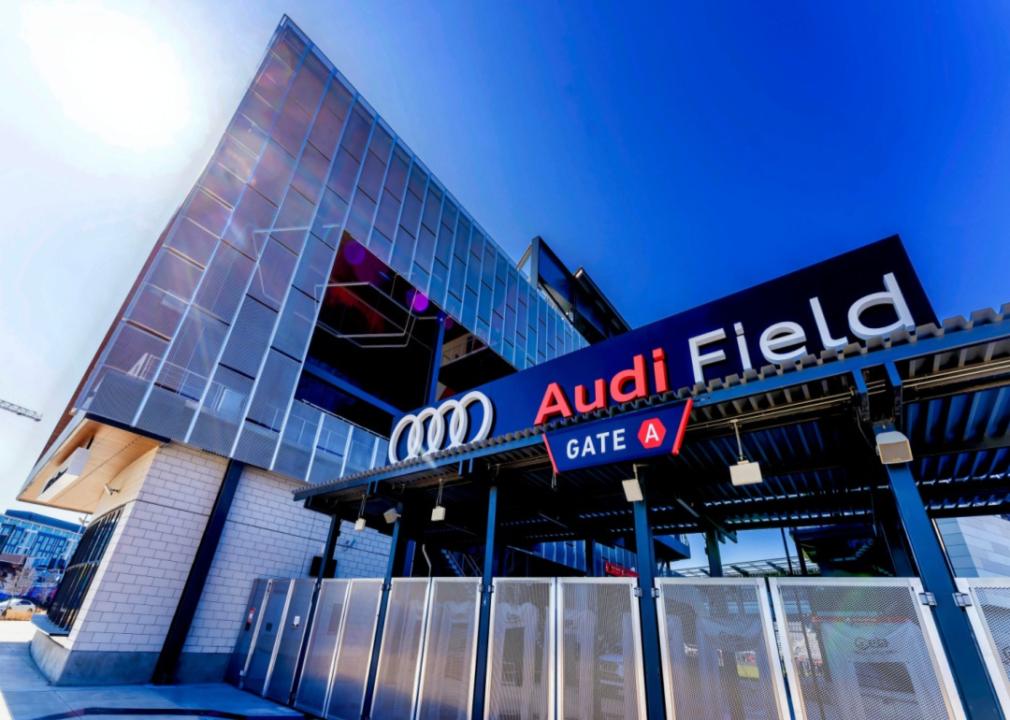 Entrance gate of Audi Field from a sidewalk looking up at the tall building in the sunlight.