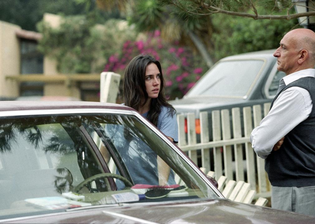 Jennifer Connelly and Ben Kingsley stand next to a car looking seriously at one another.