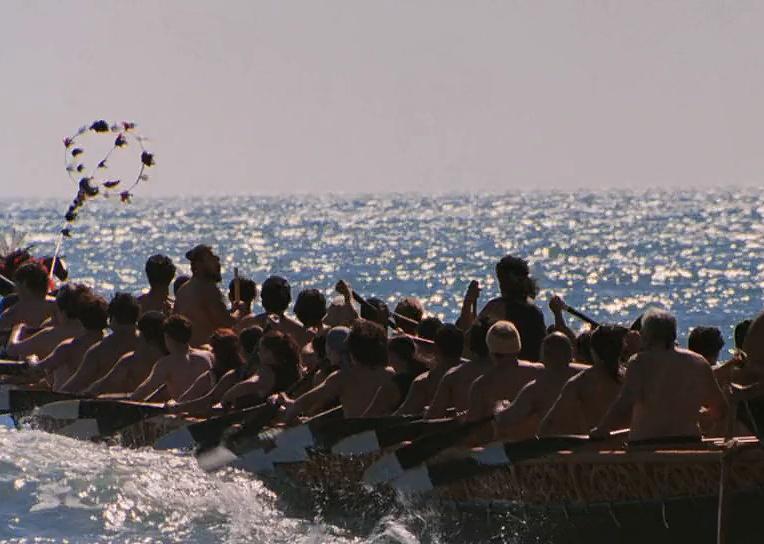A large group of people rowing in a long boat.