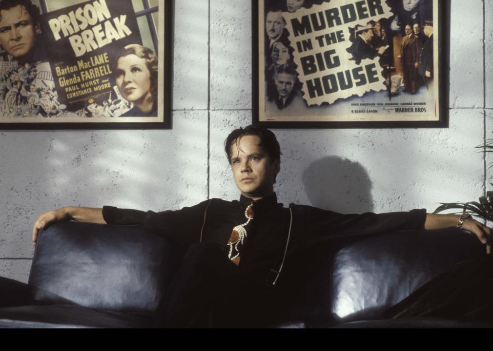 Tim Robbins sitting on a black leather couch in front of old movie posters.