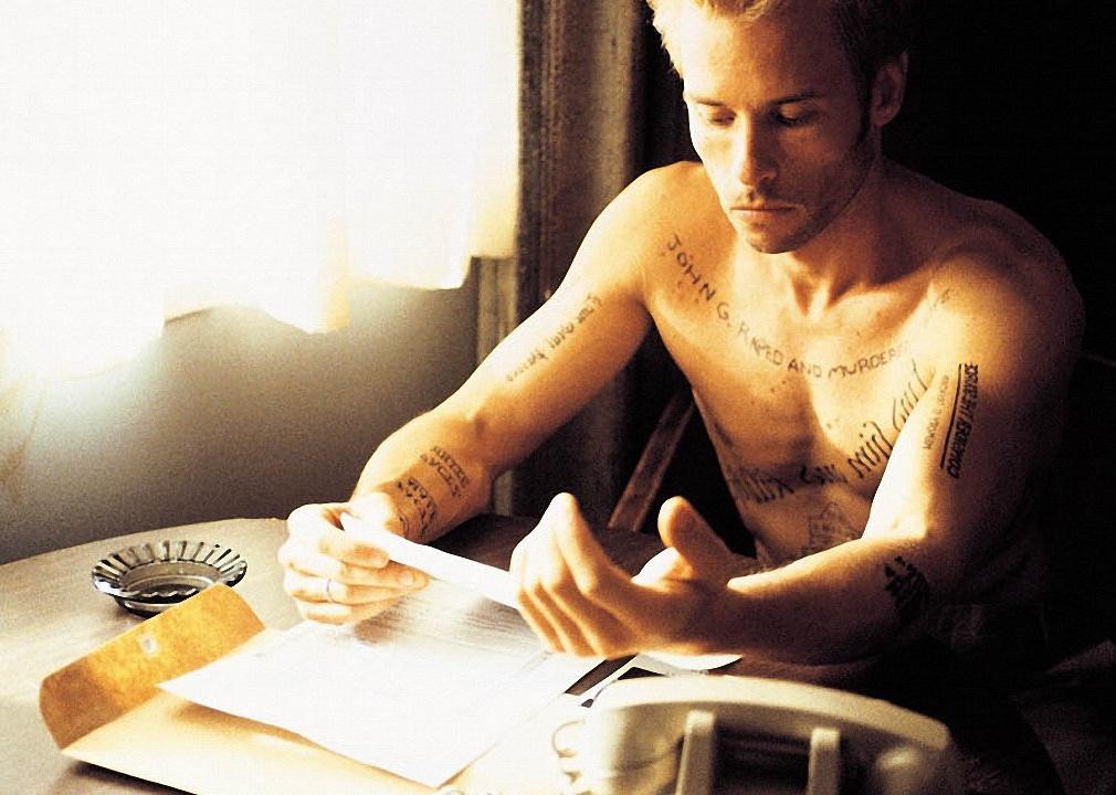 Guy Pearce looking down at tattoos all over his body.