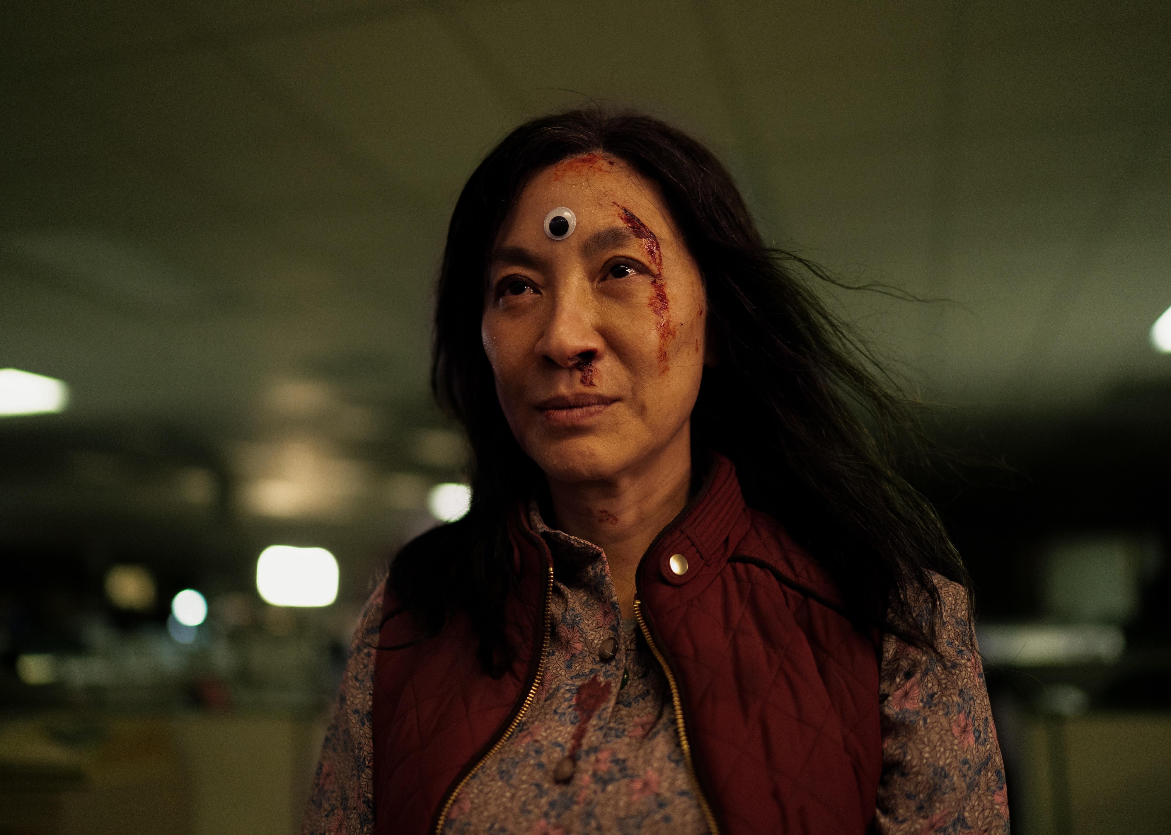 Michelle Yeoh with blood on her face and a plastic eye on her forehead.