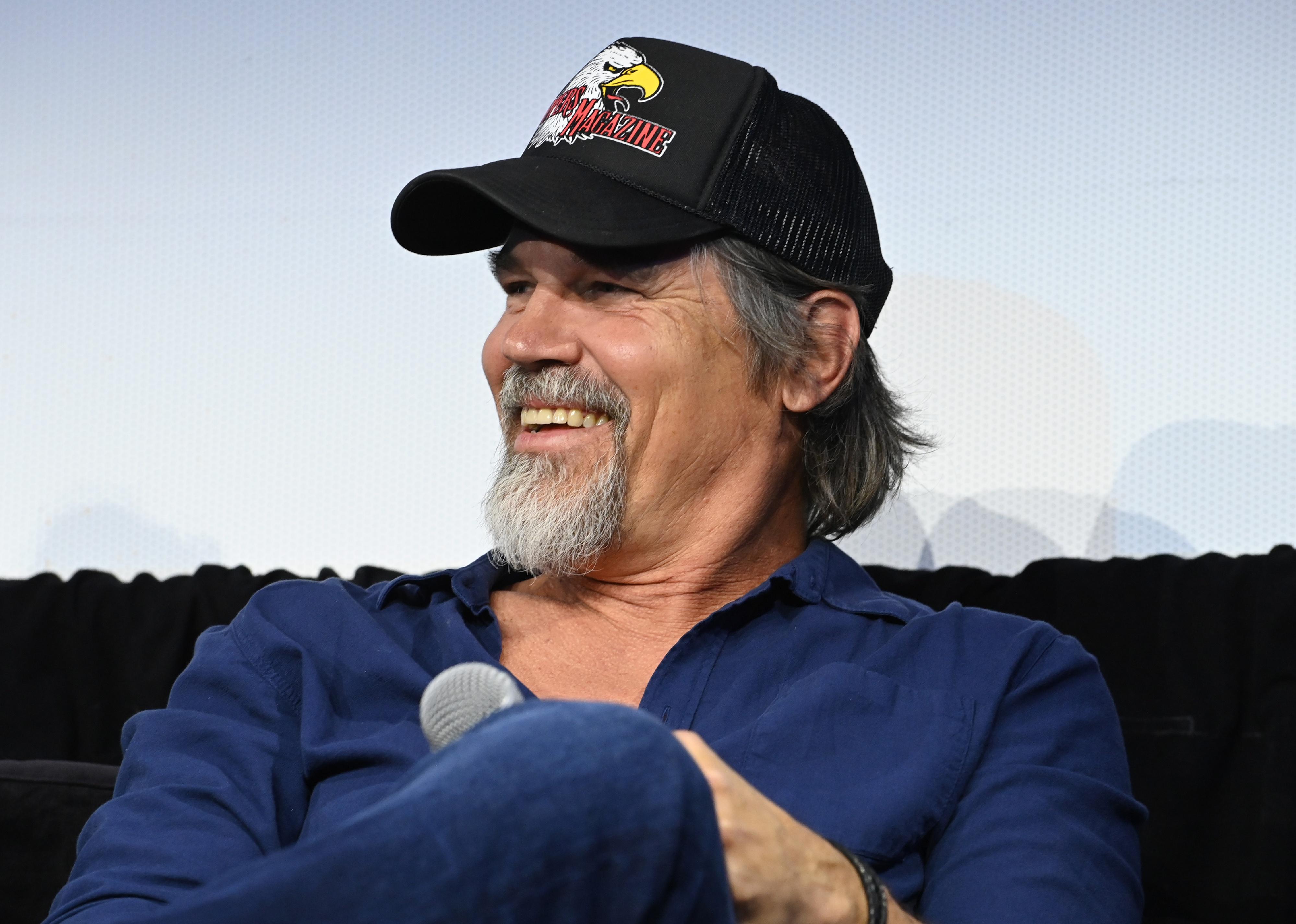 Josh Brolin onstage in a blue shirt and black trucker hat.