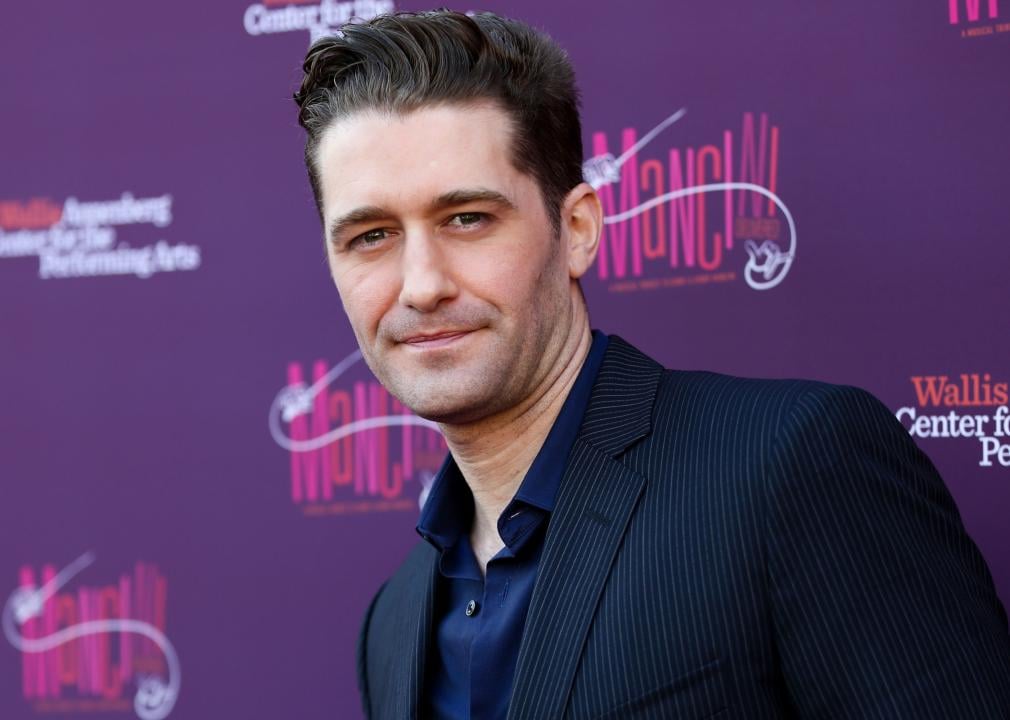Matthew Morrison poses in front of a purple background at a musical tribute.