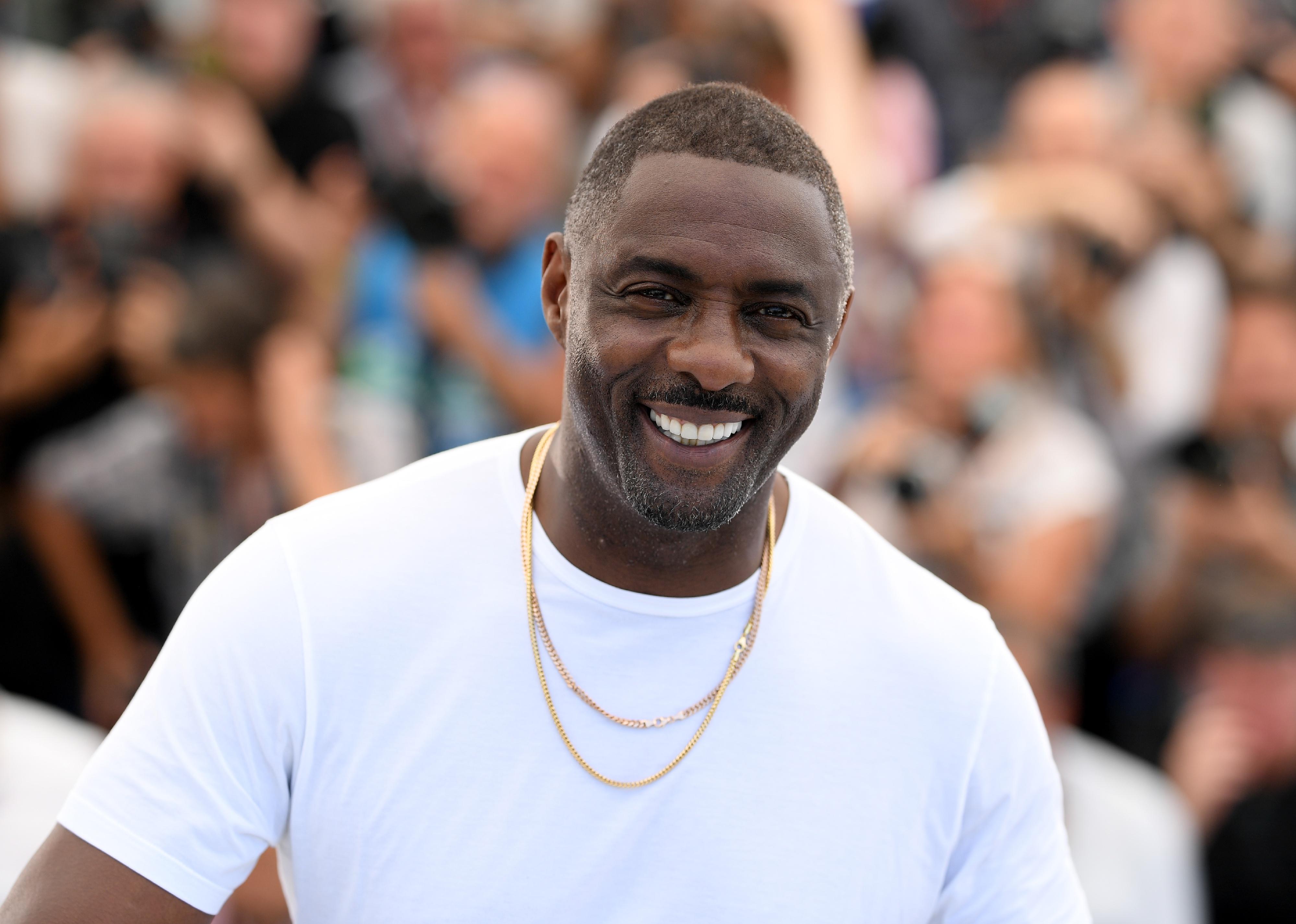 Idris Elba in a white t-shirt and gold necklaces.