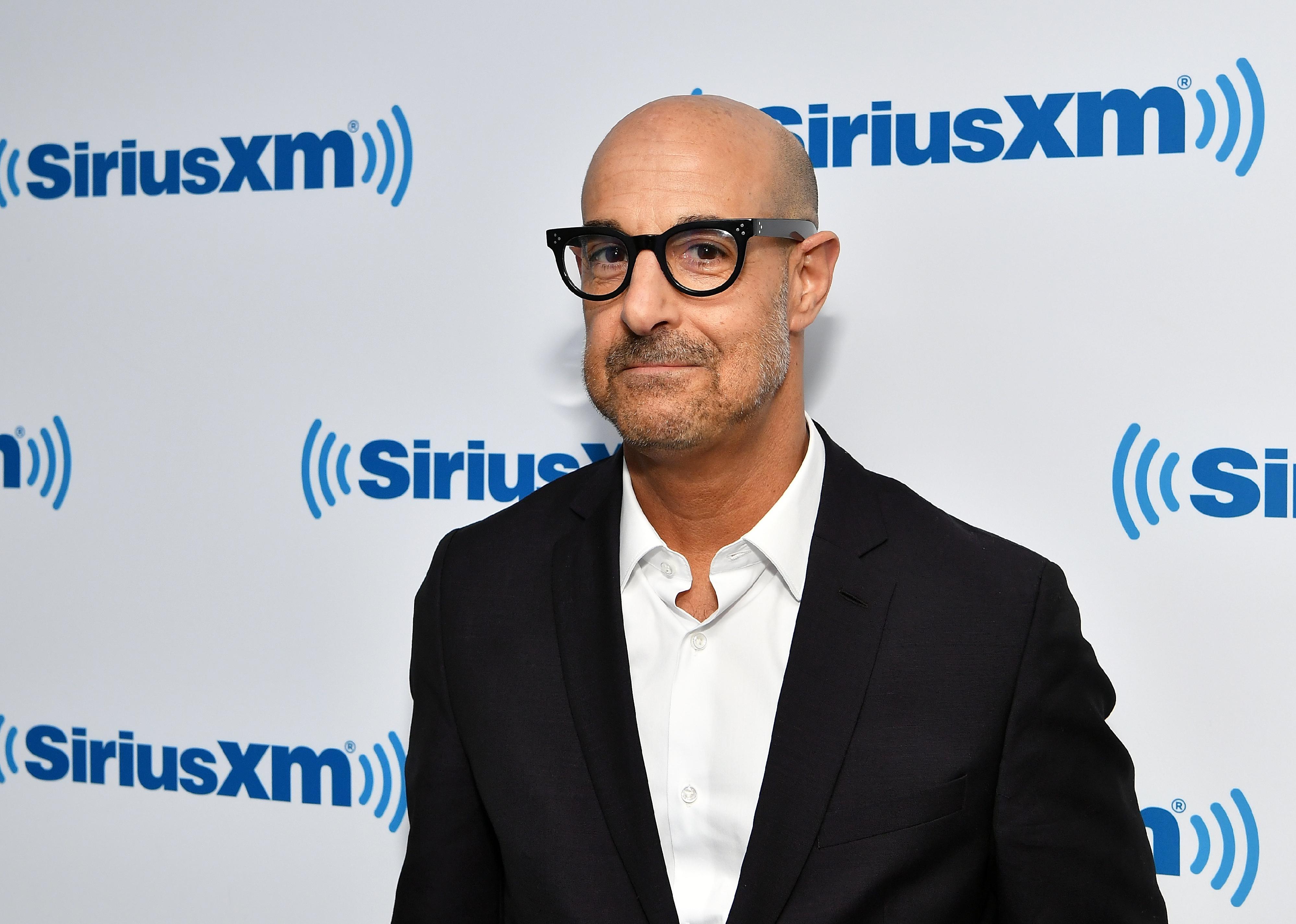 Stanley Tucci in a black blazer and glasses.