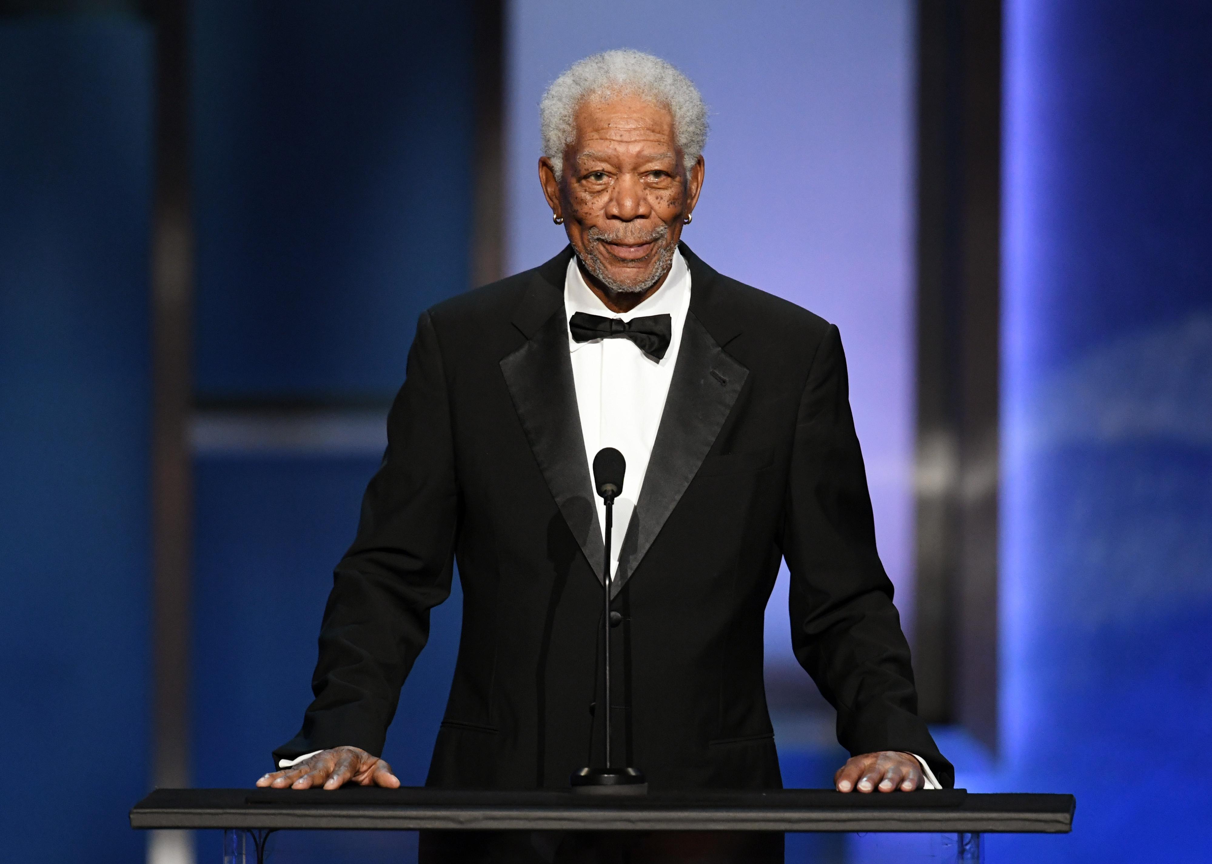 Morgan Freeman in a black suit and bowtie onstage behind a podium.