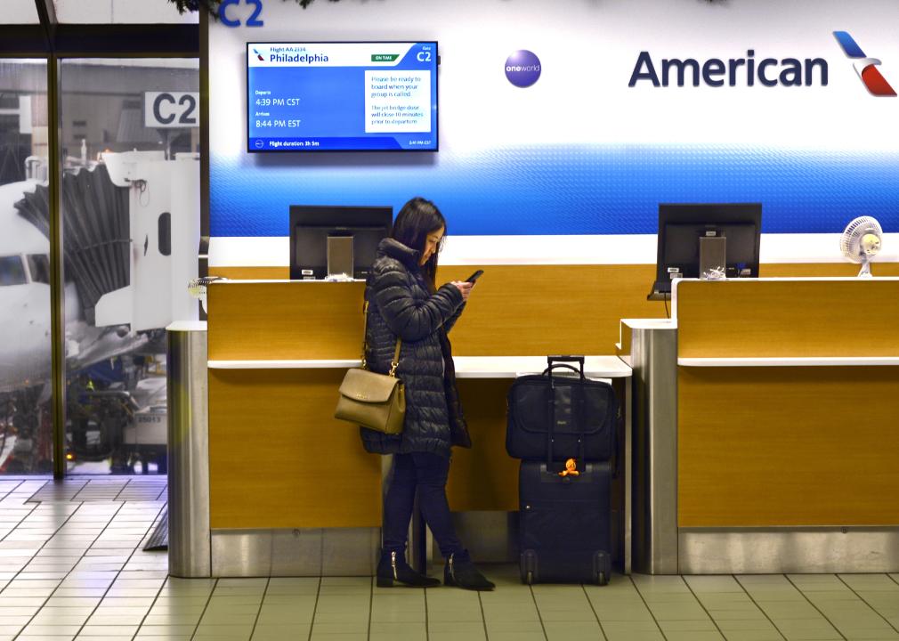 A passenger uses her smartphone in front of an American Airlines gate counter.