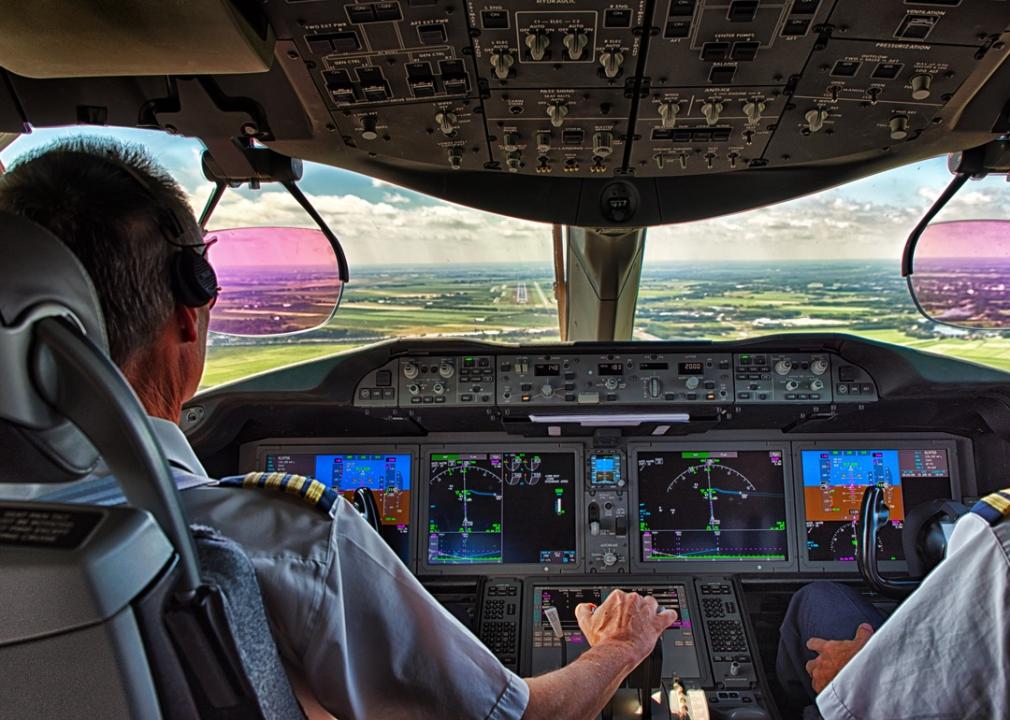 View of runway and backs of pilot and copilot from the cockpit.