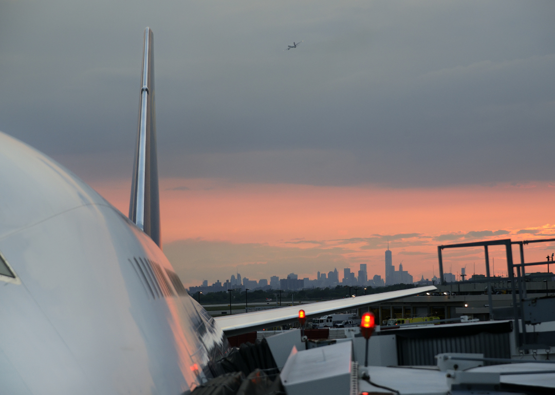 The side of an aircraft parked with the NY skyline and sunset in the background.