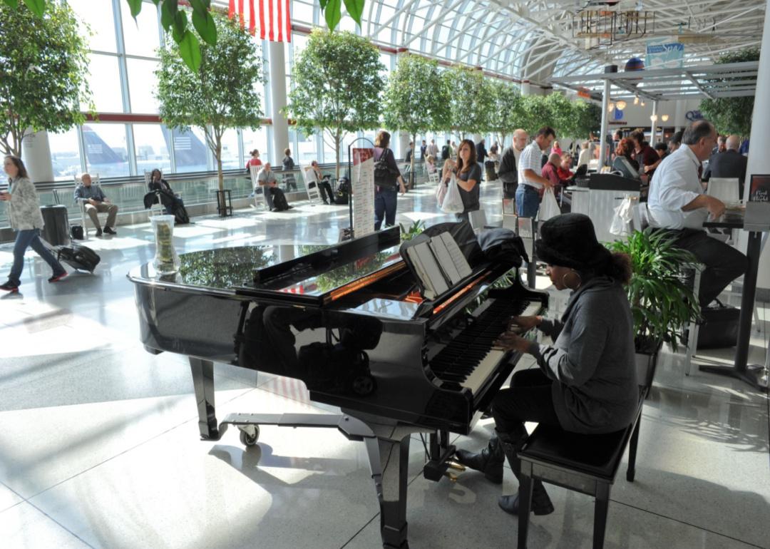 A bright atrium in the Charleston airport full of passengers in rocking chairs listening to a pianist.
