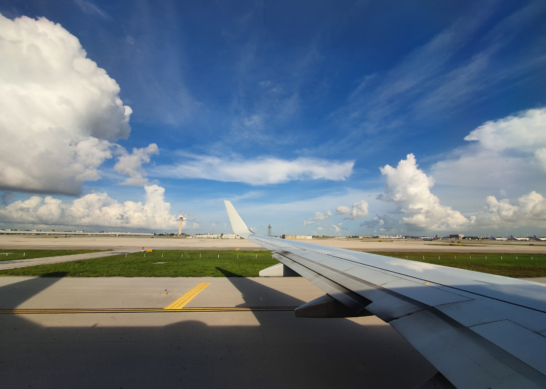 The wing of an airplane on a runway against a blue sky with clouds.