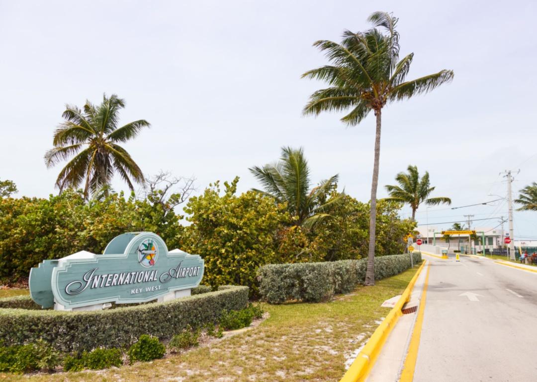 Key West airport entrance sign with palm trees lining the road.