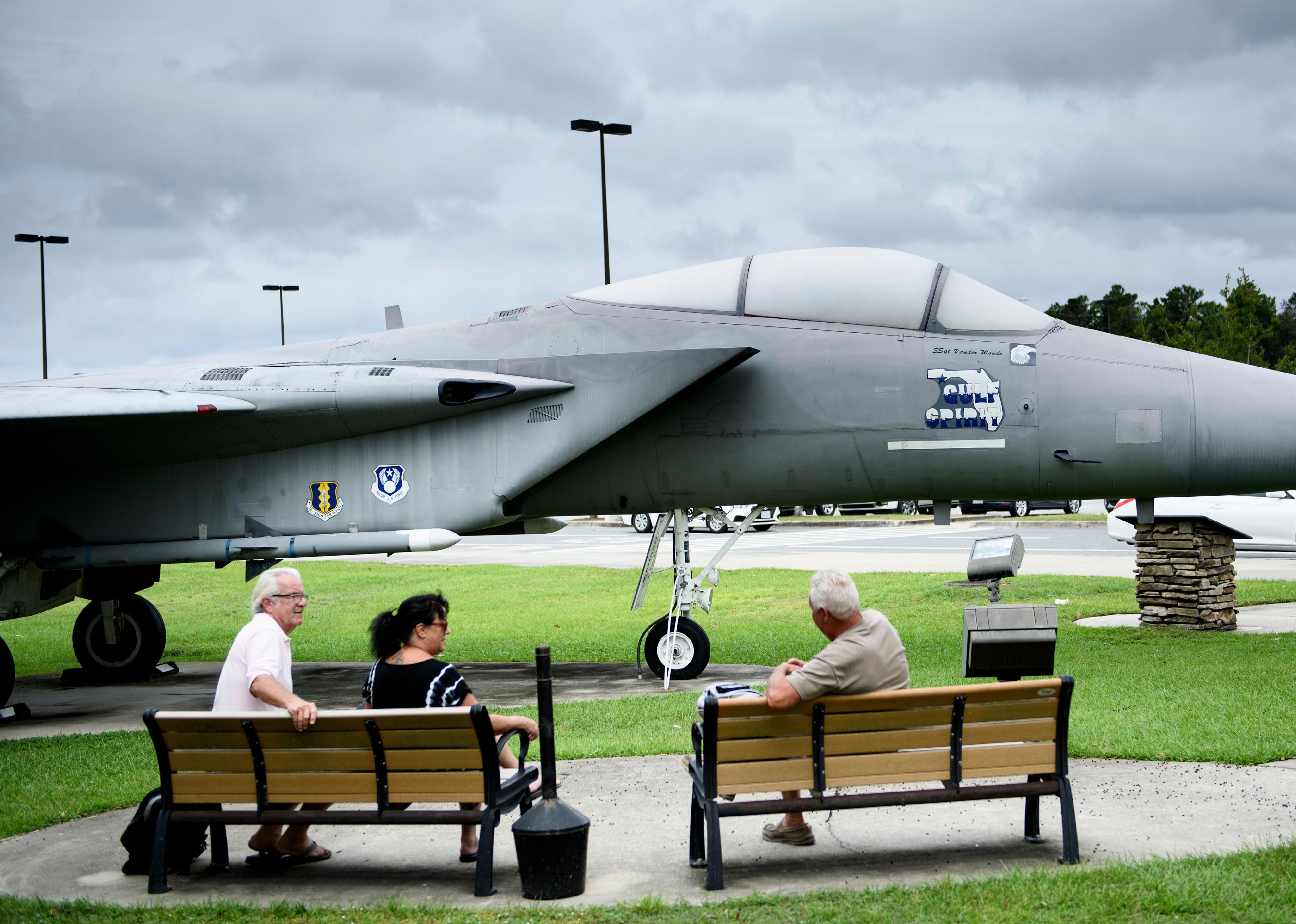 People sit on park benches in front of a military jet at Fort Walton Beach airport.