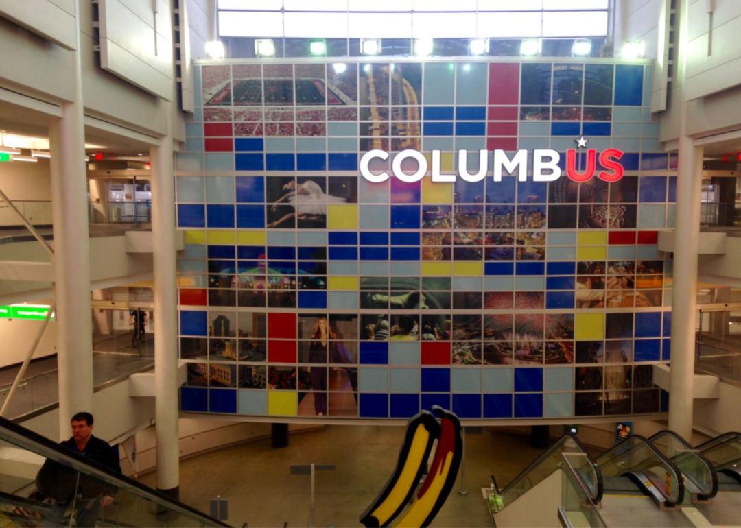 A man riding the escalator up in front of a mural at Columbus airport.