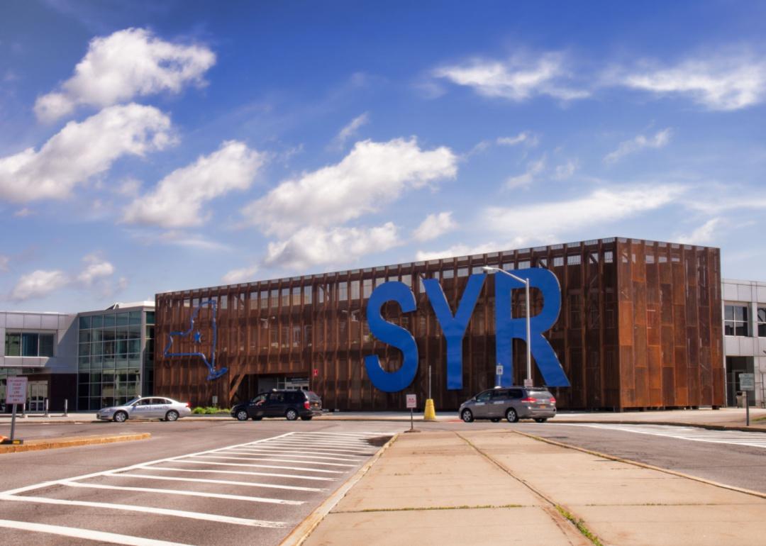 The entrance to the Syracuse Hancock airport with large blue SYR letters in blue on a building.