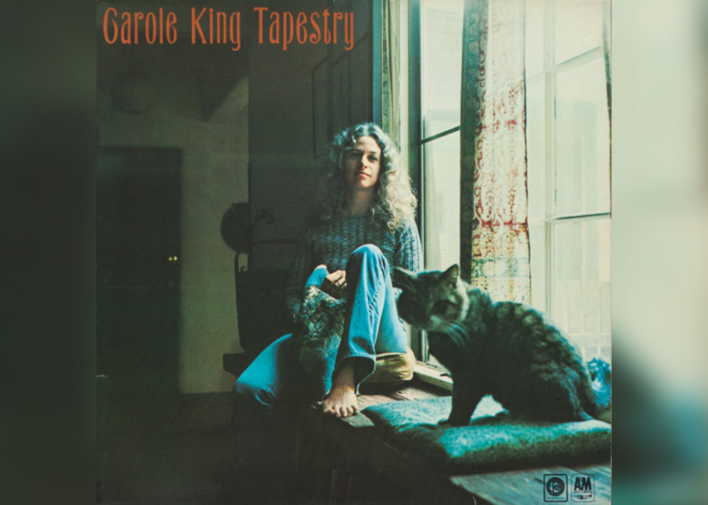 Carole King sitting in a window seat next to a cat.
