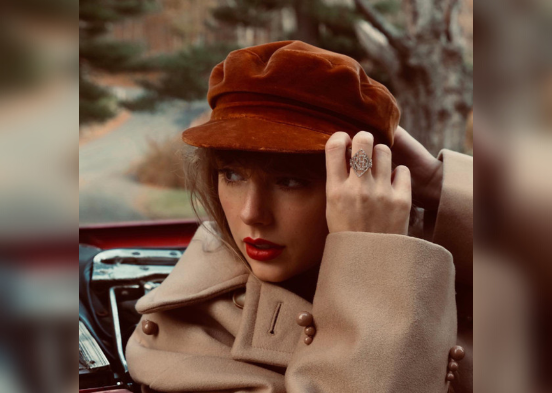 Taylor Swift wearing a brown velvet hat and tan coat.