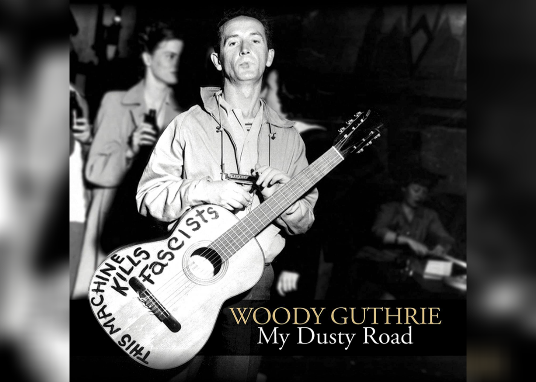 Woody Guthrie holding a guitar that reads, "This machine kills fascists" in black and white.