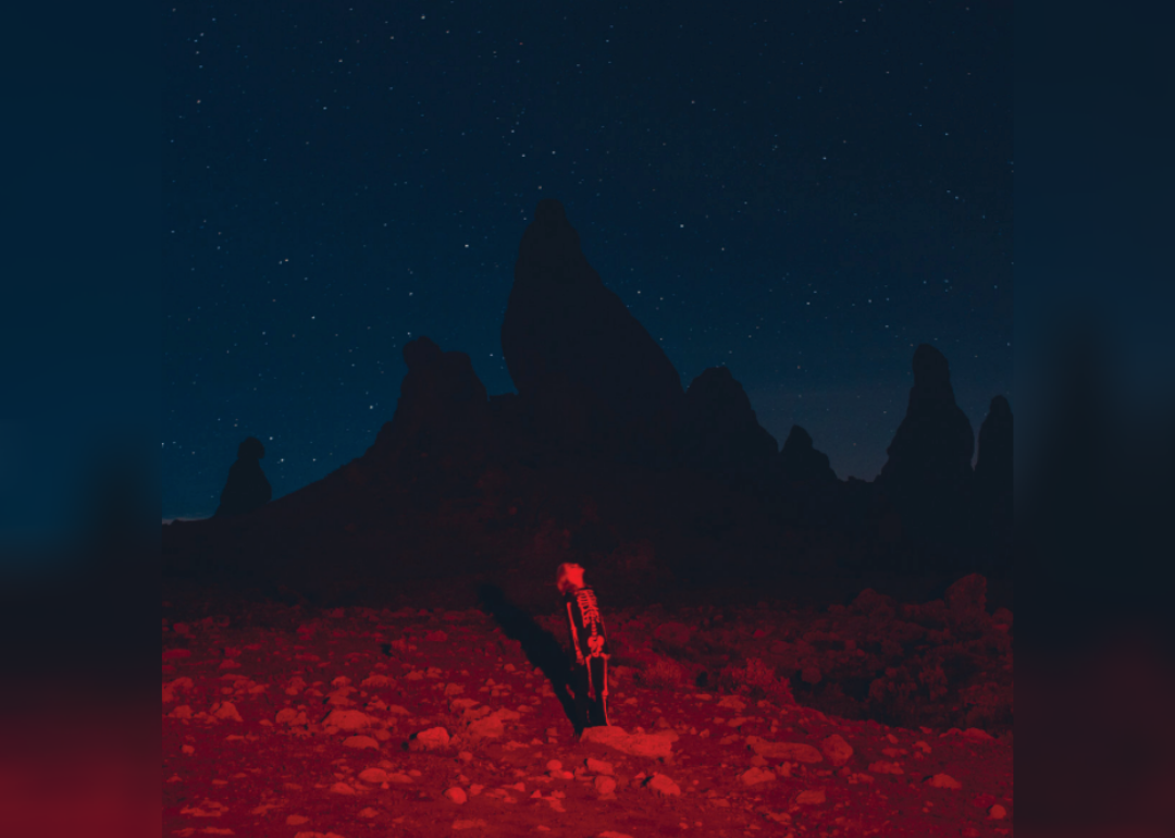 A kid under red light in a skeleton outfit looking up at the night sky.