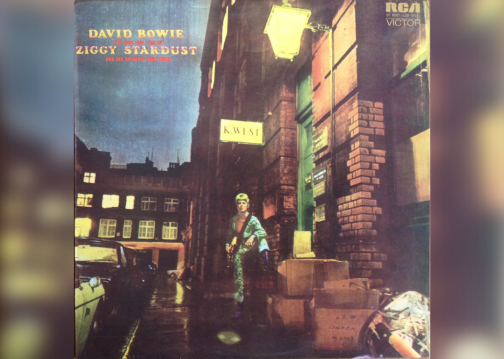 Painting of David Bowie standing on a street with a guitar and one leg up on a box.