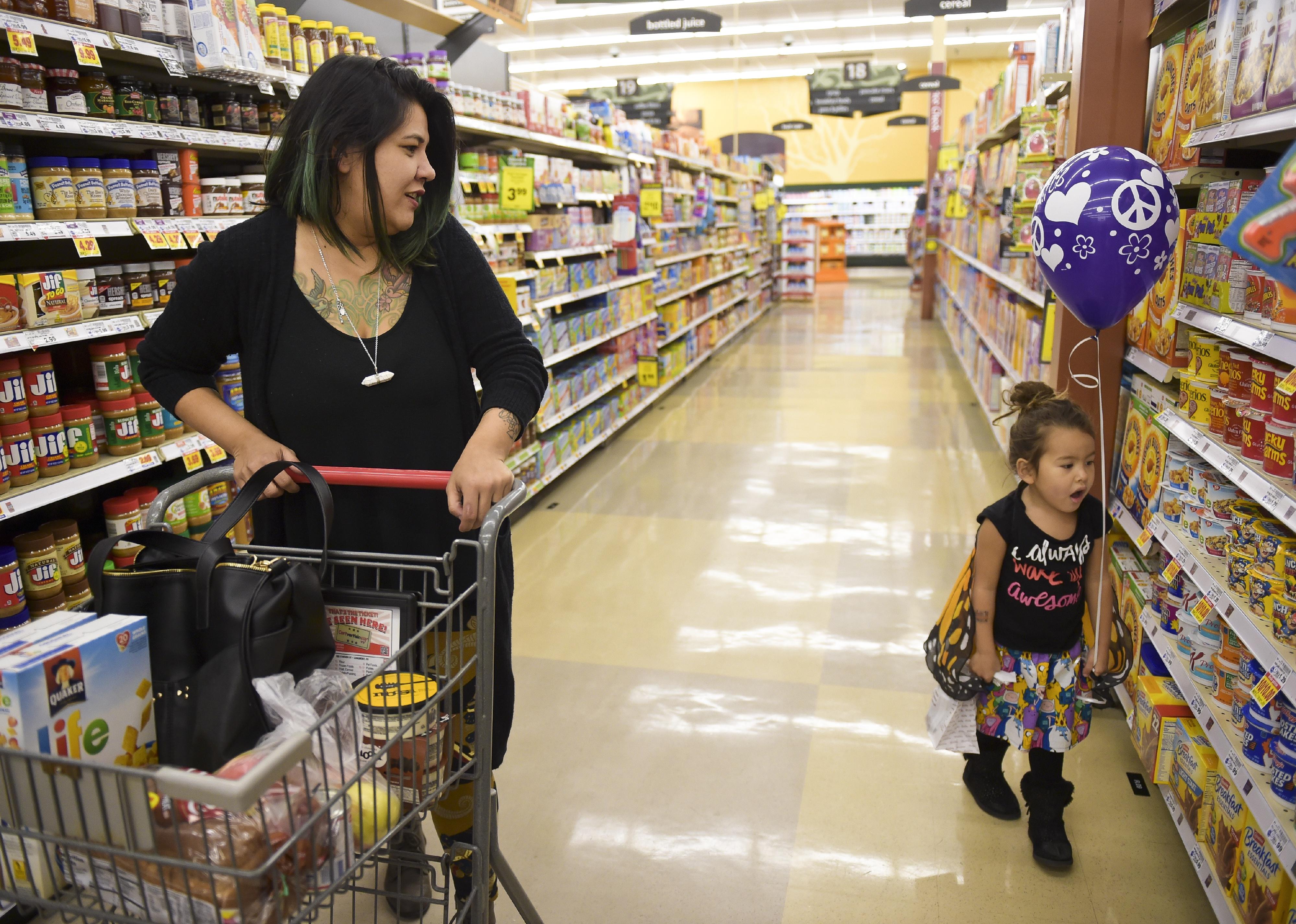 A woman pushes a grocery cart next to a little girl holding a purple balloon in the grocery store.