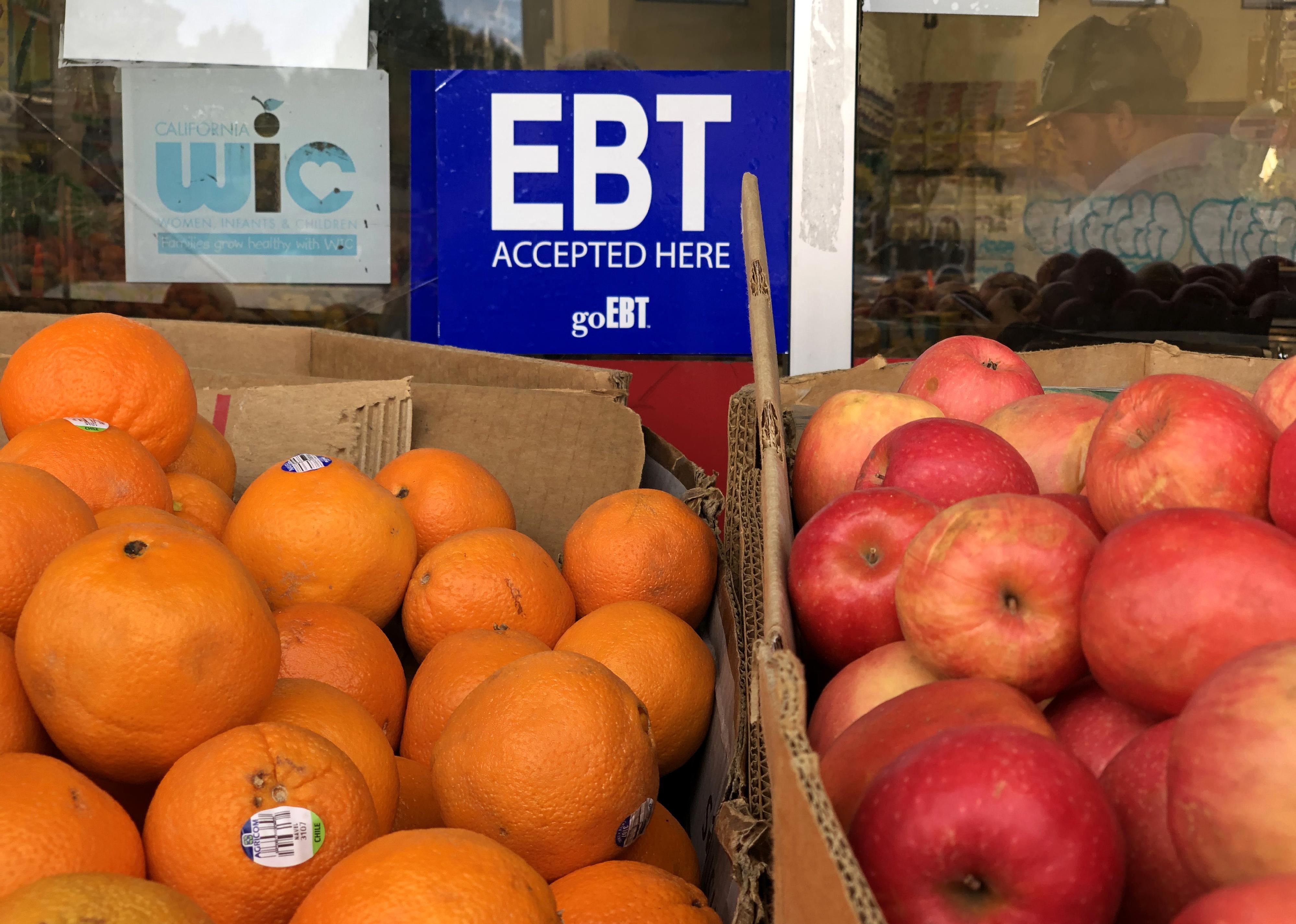 Boxes of oranges and apples in front of a store that accepts EBT cards.