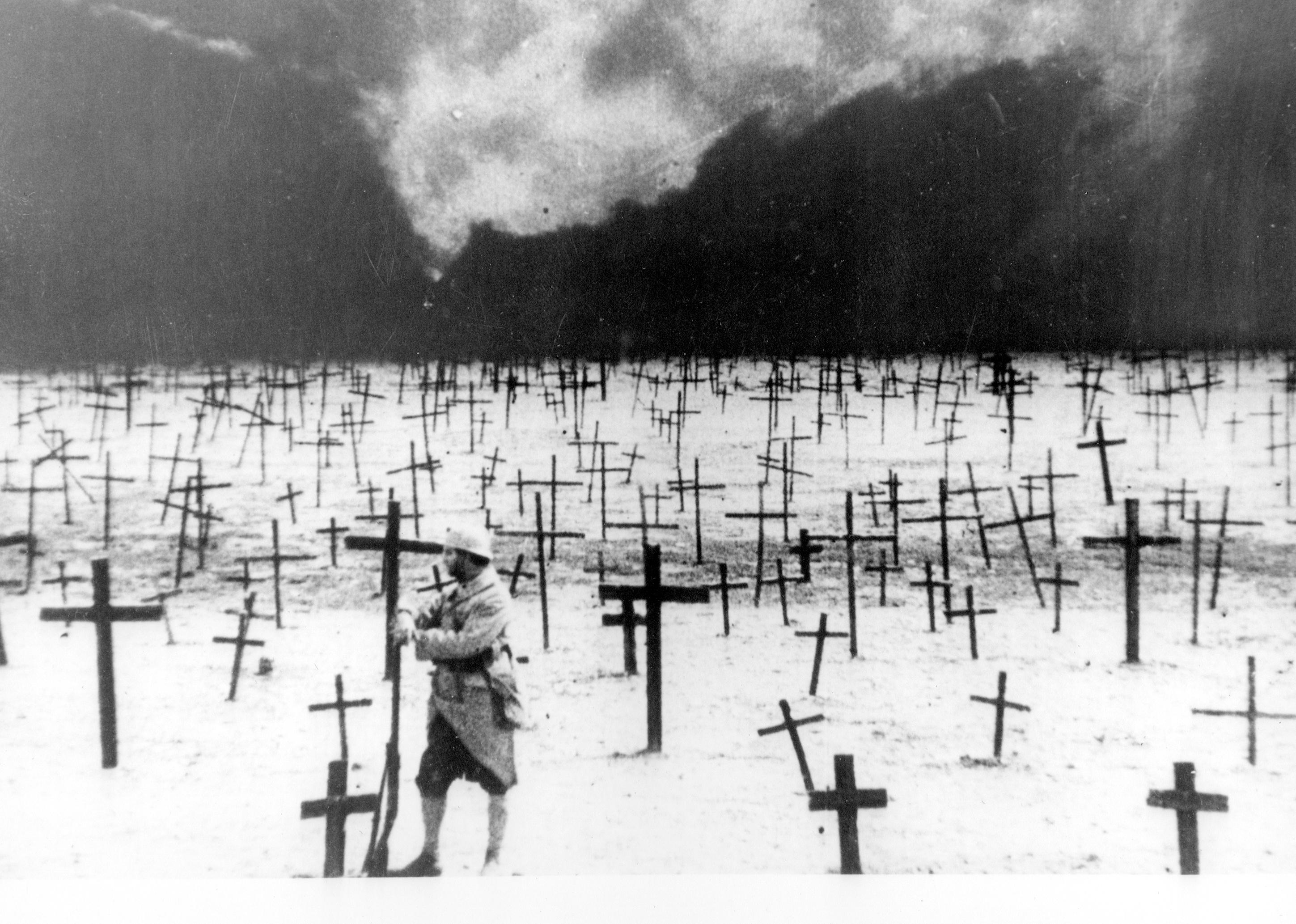 A man standing next to an endless field of crosses in the ground.