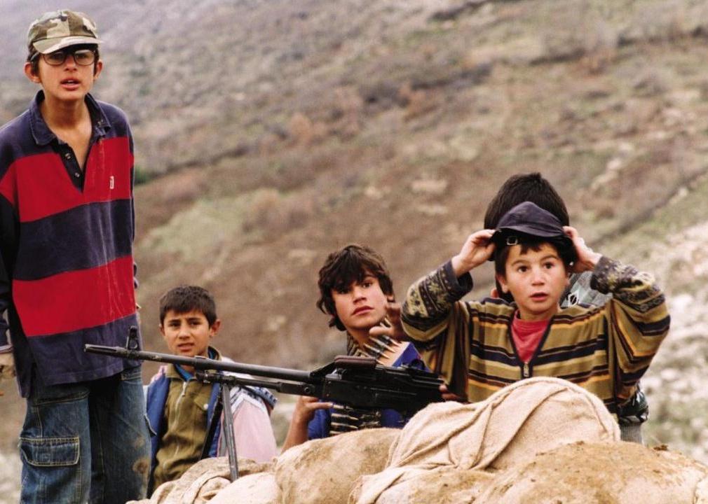 A group of young boys behind a barricade in the mountains with a large gun and ammo.