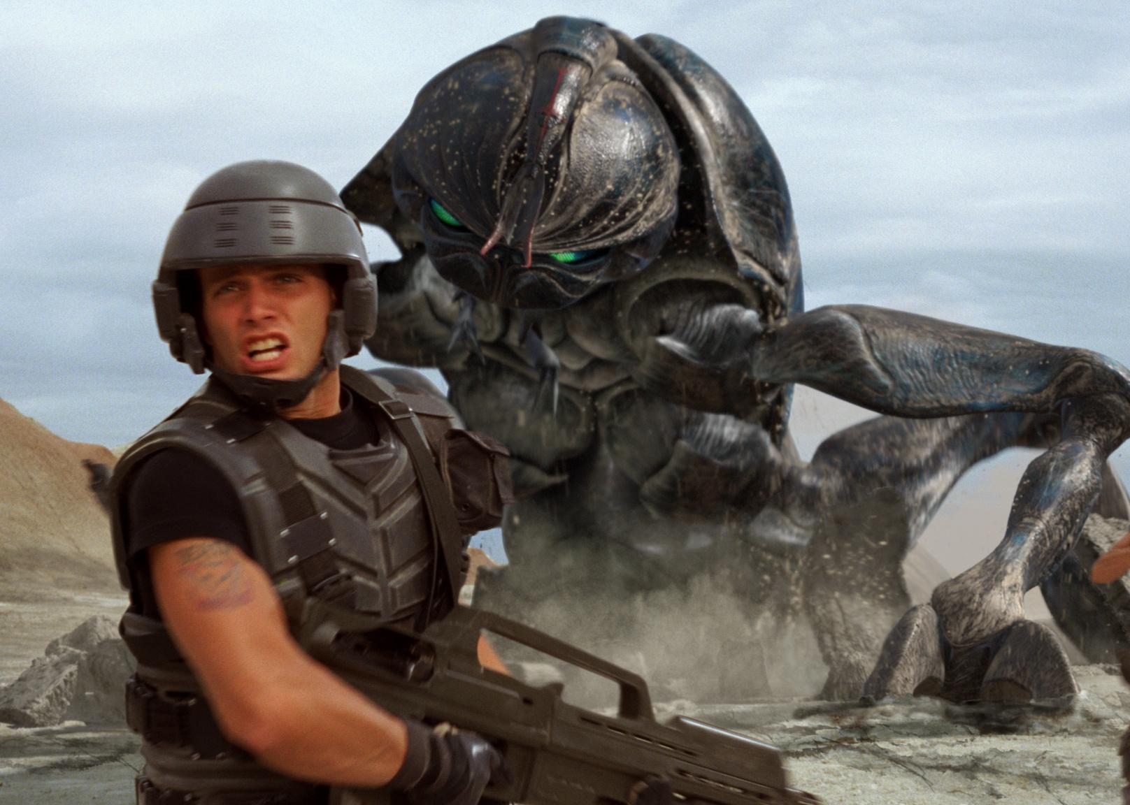 Troopers with guns running in battle with giant alien bugs behind them.