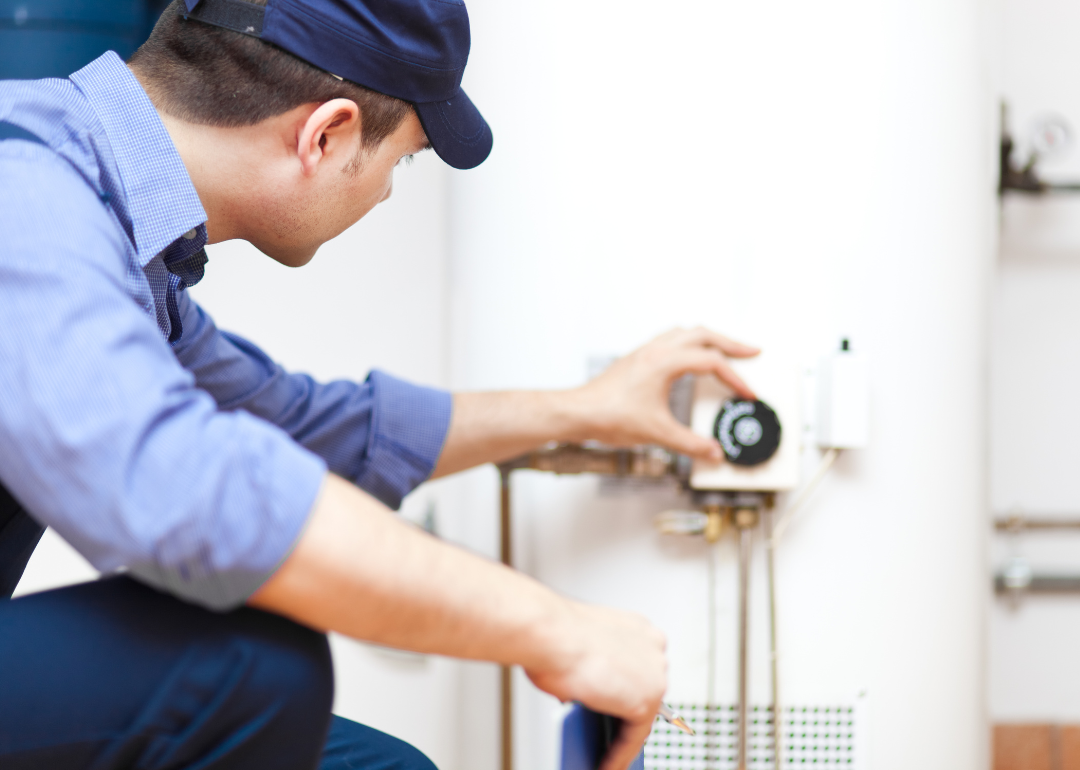 A man in a blue hat inspecting a hot water heater.