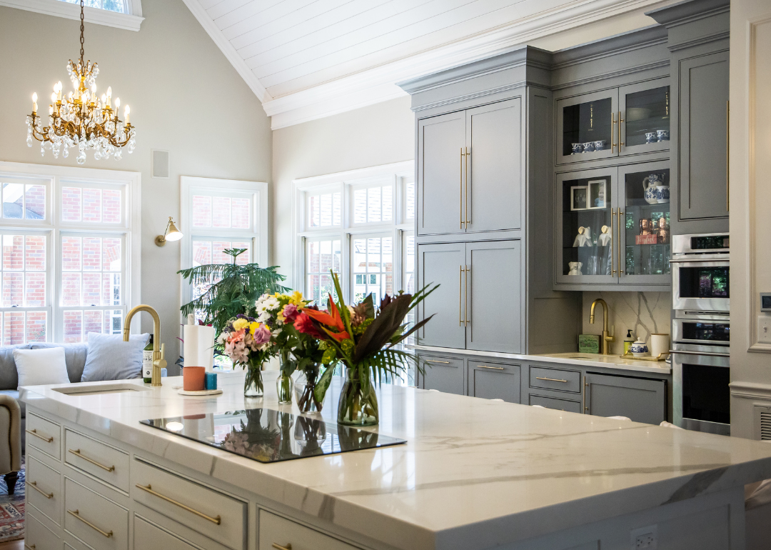 A bright kitchen with marble countertop, grey cabinets and big windows.
