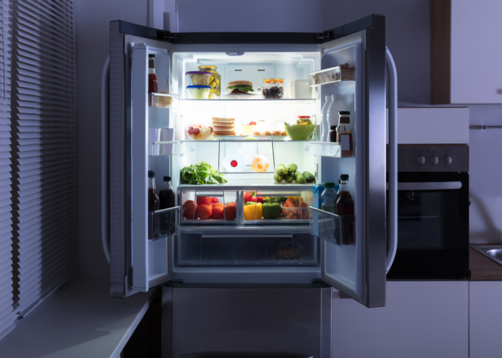 Double doors of a refrigerator open with lots of colorful food inside.
