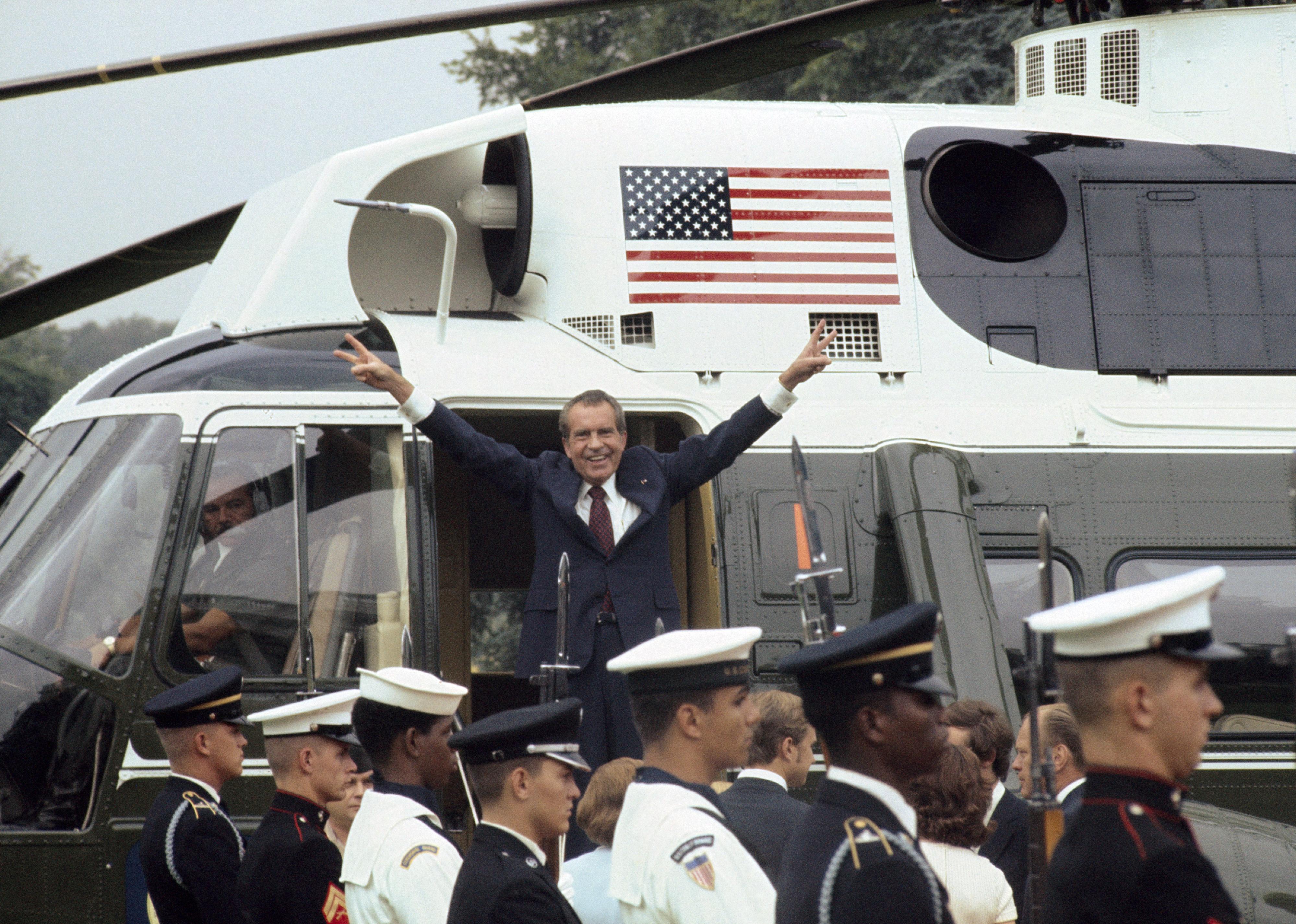 Richard Nixon standing in the White House helicopter smiling and giving the vicory sign.