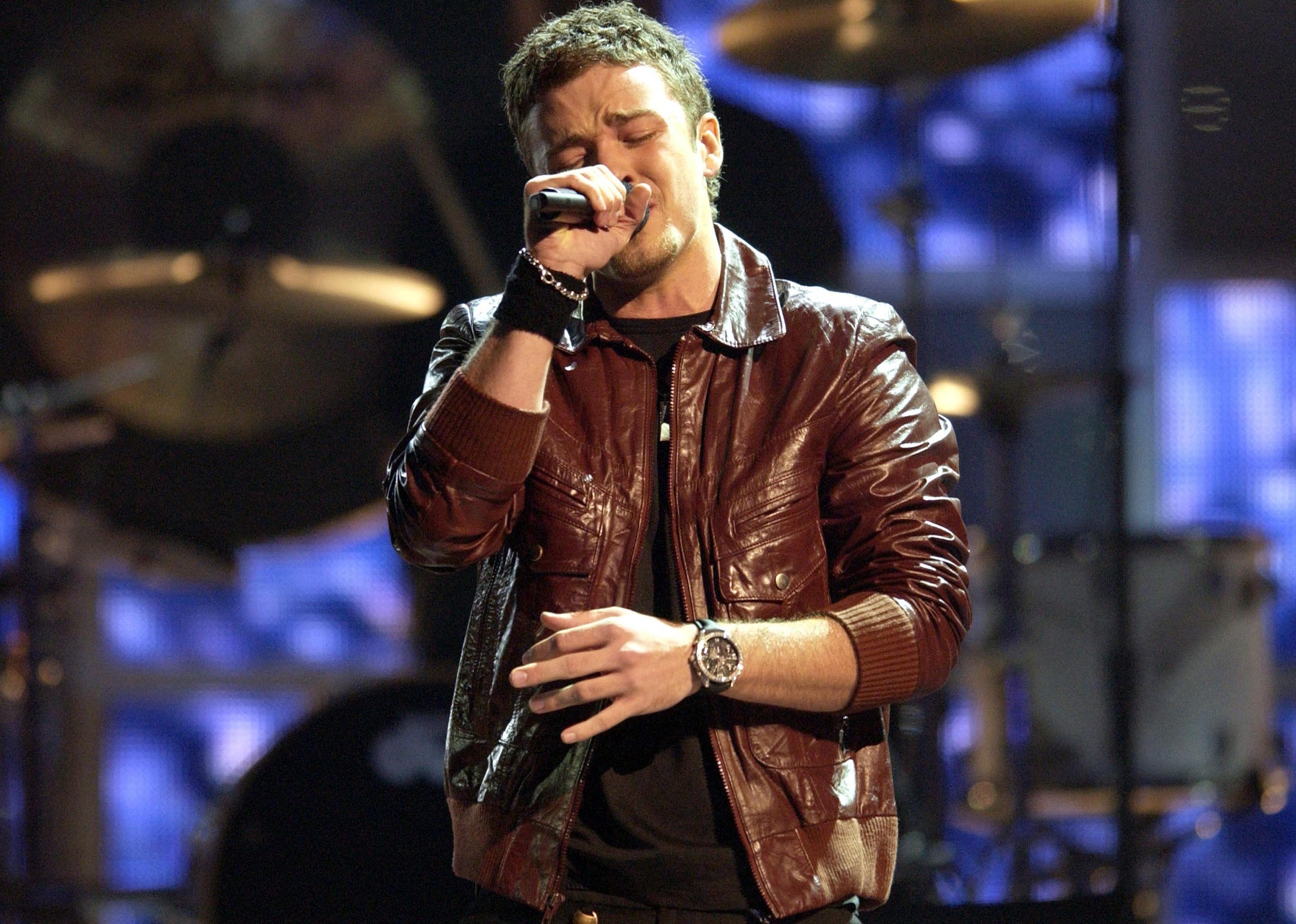 Justin Timberlake onstage wearing a brown leather jacket and singing