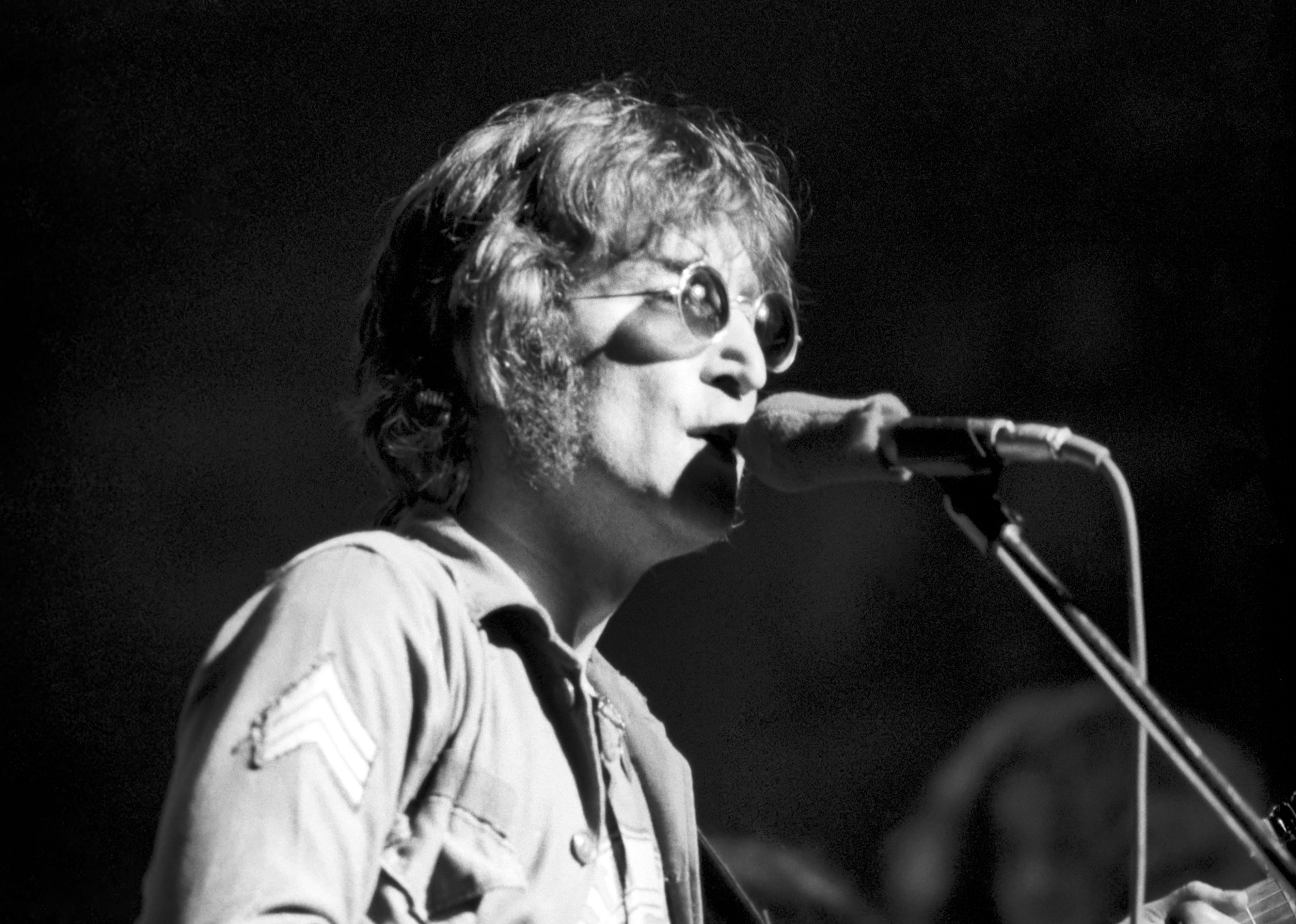 John Lennon performing in his signature round glasses and military style jacket.