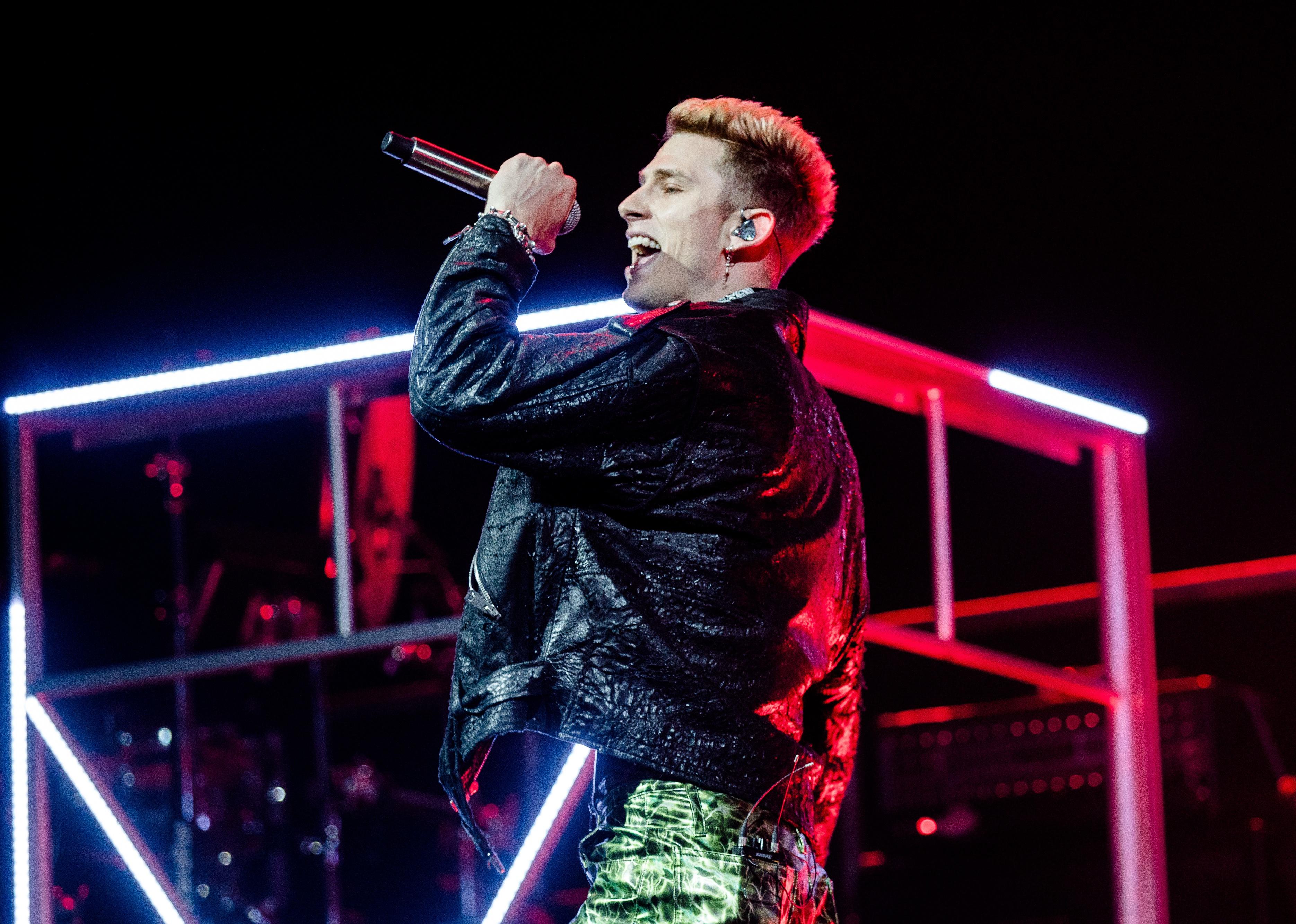Machine Gun Kelly singing in a black leather jacket and green pants.