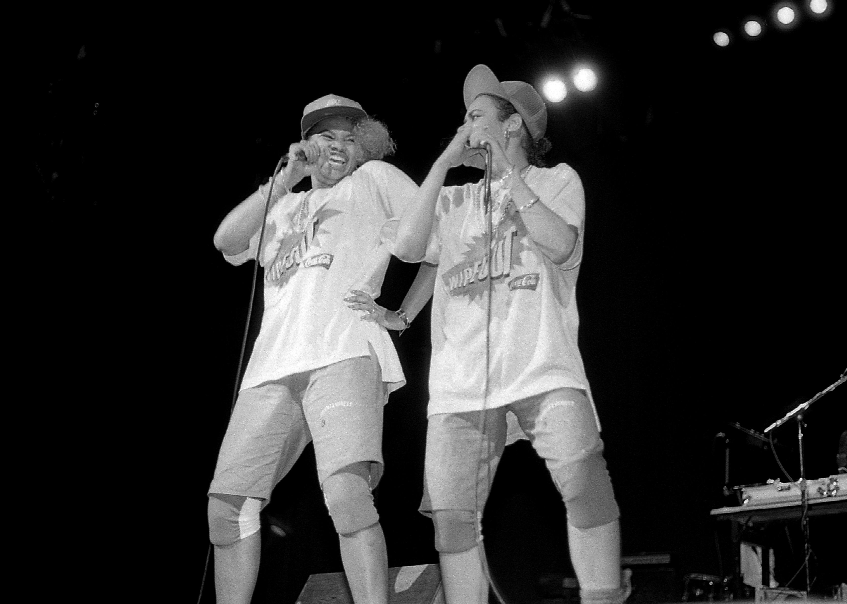 Salt-N-Pepa singing and laughing onstage in wipeout t-shirts and knee pads.