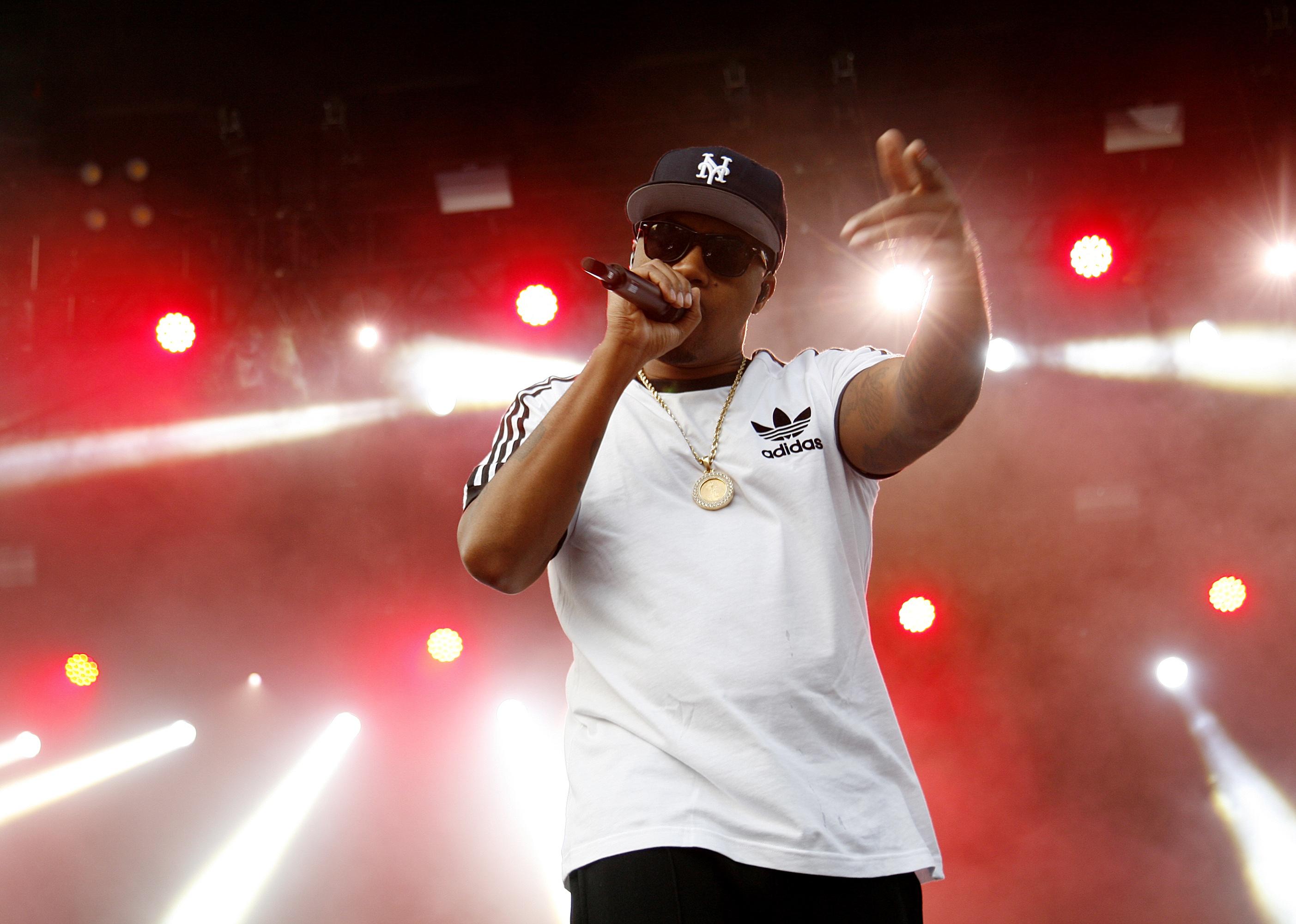 Nas performing onstage in a white adidas shirt.