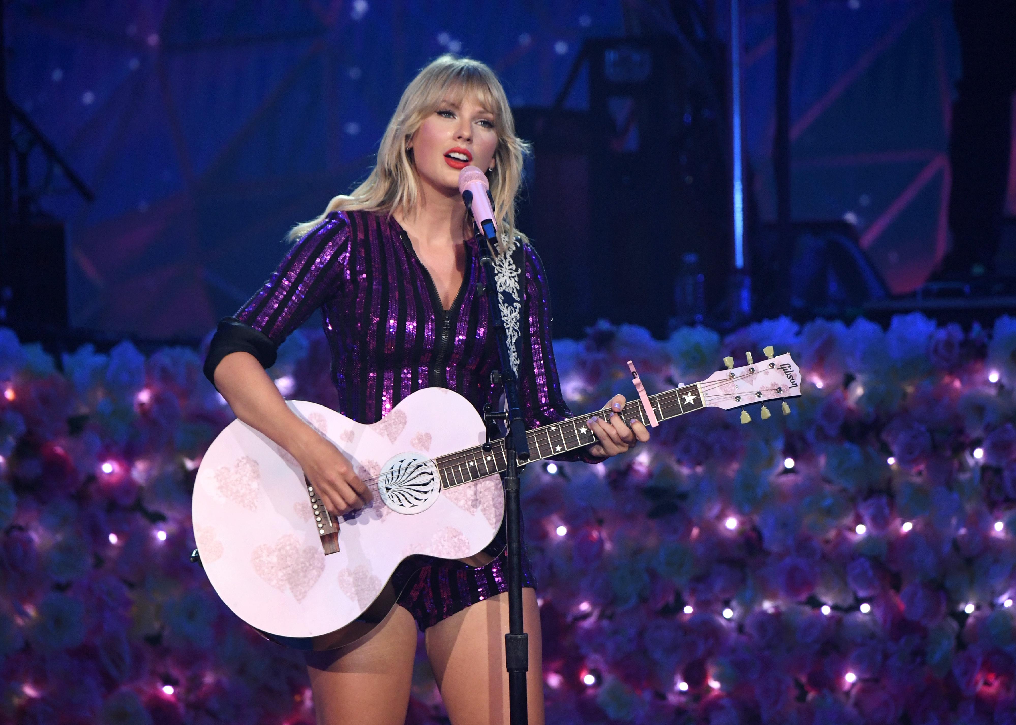 Taylor Swift in a shiny purple outfit with a pink guitar.
