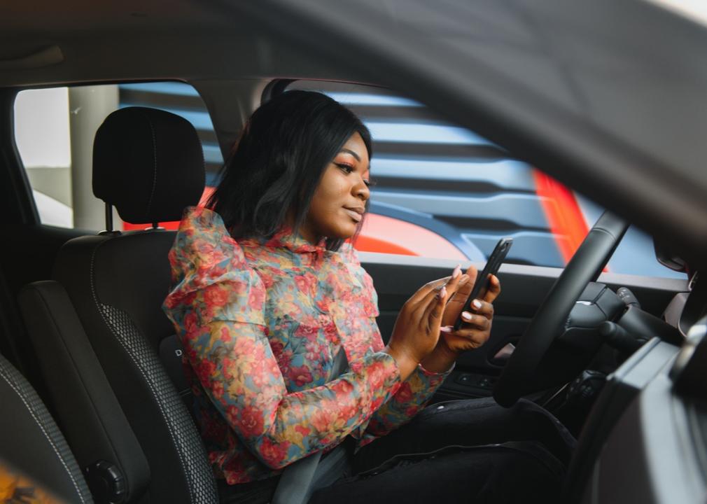 Young woman sitting in a car typing on her phone.