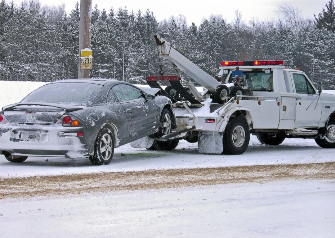 A wrecked car being towed in the snow.