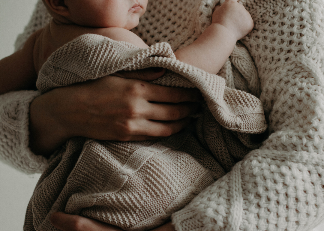 A person holding a baby in a brown blanket.