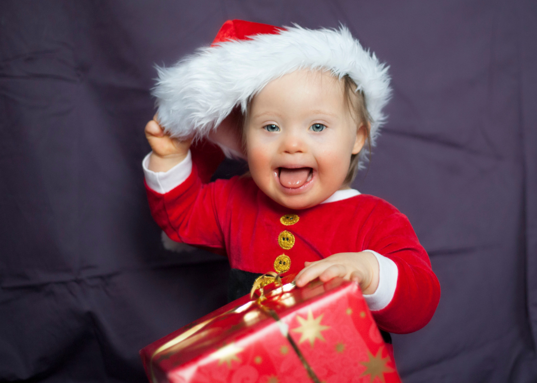 A baby in a red Christmas suit holding a present.