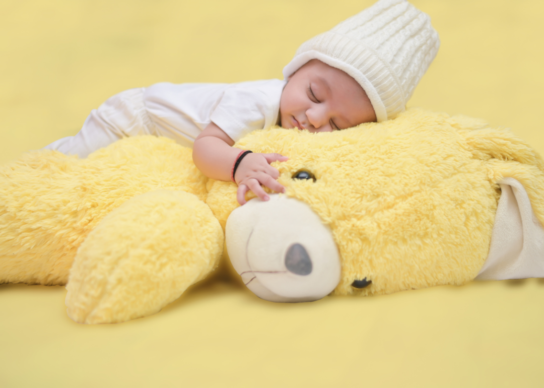 A baby in a white outfit sleeping on a yellow bear.