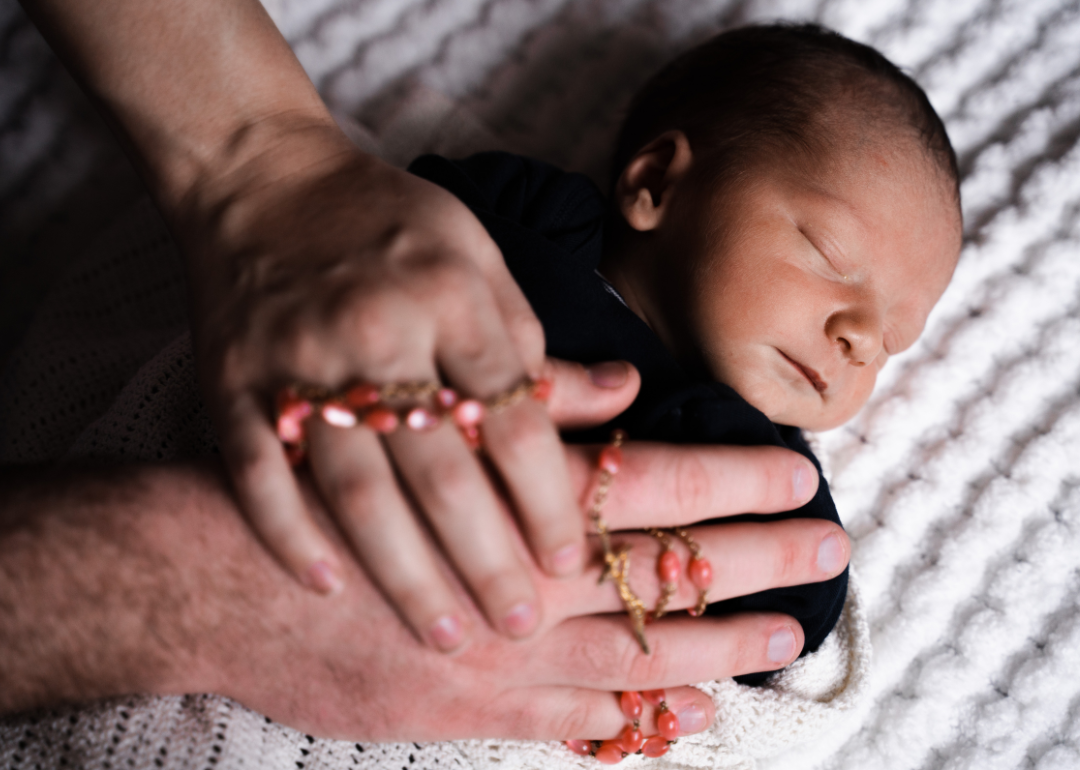 Adult hands resting on a sleeping baby.