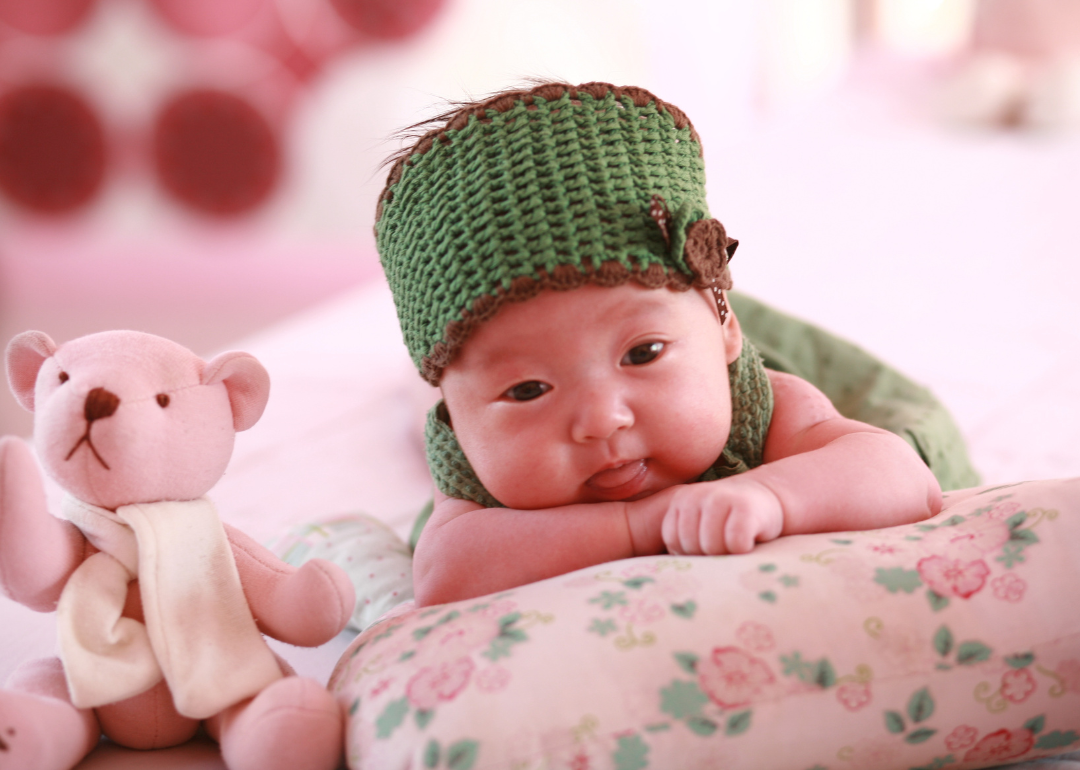 A baby on a floral pillow wearing a green hat and outfit.